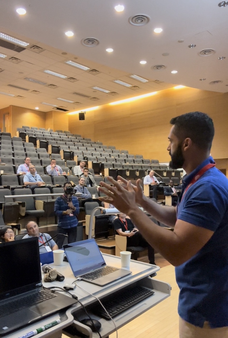 Mustapha in a blue shirt speaking to an audience in an auditorium